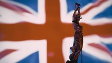 The Statue Of Justice - Lady Justice, British Justice System. Justitia The Roman Goddess Of Justice In Front Of UK Flag