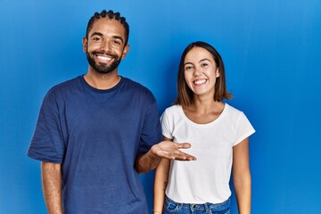 Sticker - Young hispanic couple standing together smiling cheerful presenting and pointing with palm of hand looking at the camera.