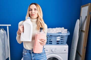 Wall Mural - Young caucasian doctor woman holding detergent bottle at laundry room smiling looking to the side and staring away thinking.