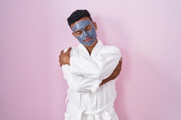 Sticker - Young hispanic man wearing beauty face mask and bath robe hugging oneself happy and positive, smiling confident. self love and self care