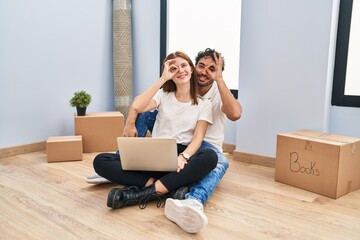 Canvas Print - Young couple using laptop at new home doing ok gesture with hand smiling, eye looking through fingers with happy face.