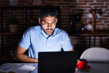 Wall Mural - Hispanic man with beard using laptop at night with hand on stomach because indigestion, painful illness feeling unwell. ache concept.