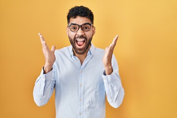 Poster - Hispanic man with beard standing over yellow background celebrating crazy and amazed for success with arms raised and open eyes screaming excited. winner concept