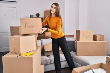 Sticker - Young caucasian woman smiling confident holding fragile package at new home