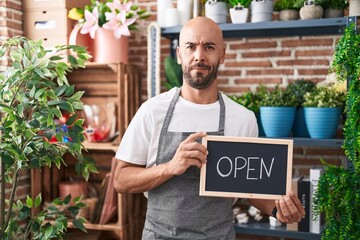 Sticker - Middle age bald man working at florist holding open sign clueless and confused expression. doubt concept.