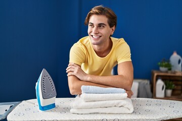 Wall Mural - Young caucasian man smiling confident leaning on ironing board at laundry room