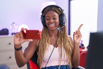 Poster - African american woman with braided hair playing video games with smartphone smiling happy pointing with hand and finger to the side