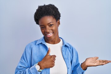 Sticker - African american woman standing over blue background showing palm hand and doing ok gesture with thumbs up, smiling happy and cheerful