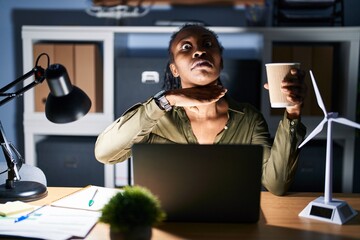 Wall Mural - African woman working using computer laptop at night cutting throat with hand as knife, threaten aggression with furious violence