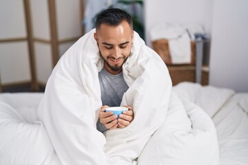 Sticker - Young hispanic man drinking cup of coffee sitting on bed at bedroom