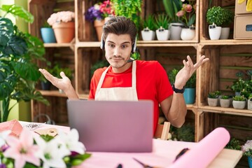 Sticker - Young hispanic man working at florist shop doing video call shouting and screaming loud to side with hand on mouth. communication concept.