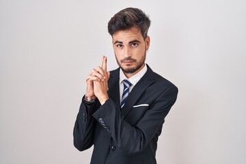 Sticker - Young hispanic man with tattoos wearing business suit and tie holding symbolic gun with hand gesture, playing killing shooting weapons, angry face