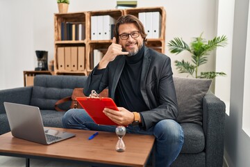 Wall Mural - Handsome middle age man working at consultation office smiling doing phone gesture with hand and fingers like talking on the telephone. communicating concepts.