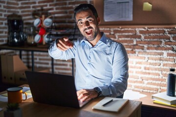 Sticker - Hispanic man with beard working at the office at night pointing to you and the camera with fingers, smiling positive and cheerful