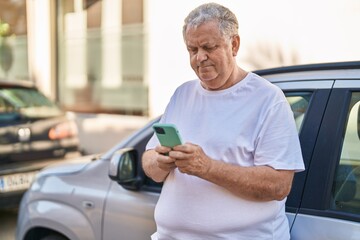 Canvas Print - Middle age grey-haired man using smartphone leaning on car at street