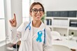 © Krakenimages.com - Young brunette doctor woman wearing stethoscope at the clinic showing and pointing up with finger number one while smiling confident and happy.