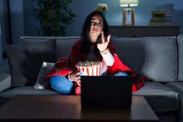 Canvas Print - Hispanic woman eating popcorn watching a movie on the sofa showing middle finger, impolite and rude fuck off expression