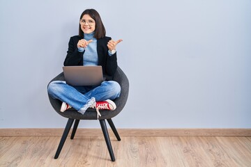 Sticker - Young hispanic woman sitting on chair using computer laptop pointing to the back behind with hand and thumbs up, smiling confident