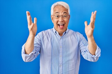 Poster - Hispanic senior man wearing glasses celebrating crazy and amazed for success with arms raised and open eyes screaming excited. winner concept