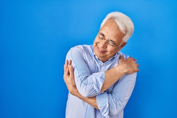 Poster - Hispanic senior man wearing glasses hugging oneself happy and positive, smiling confident. self love and self care