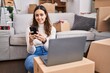 © Krakenimages.com - Young beautiful hispanic woman using laptop and smartphone sitting on floor at new home