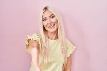 Sticker - Caucasian woman standing over pink background smiling friendly offering handshake as greeting and welcoming. successful business.