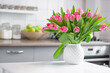 a bouquet of tulips in a white vase stand on the kitchen table. Kitchen background