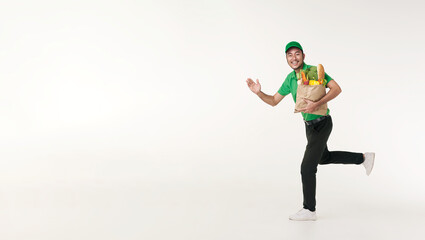 Wall Mural - Asian delivery man wearing in green uniform holding fresh food paper bag and running isolated over white background. express delivery concept.