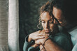 © simona - Love and relationship with young mature man and woman at home in romantic indoor leisure activity together. One adult man hug bonding serene woman in front of a window. Romance and people embrace