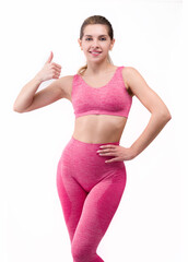 Wall Mural - Fitness woman with athletic figure standing on white background showing finger up .Fit woman in pink sportswear isolated on white background smiling showing okay or okay.In a pink outfit
