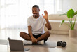 © Prostock-studio - Cheerful african sportsman waving at laptop screen, home interior