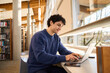© Maria Vitkovska - Smart Hispanic male student sitting at desk and using laptop preparing diploma project in the library campus