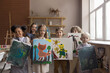© fizkes - Diverse group of happy proud kids attending artistic school class, standing together, holding canvas, showing painted pictures, looking at camera, smiling, laughing, studying creativity, art