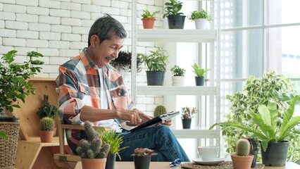 Wall Mural - Cheerful elderly Asian man relaxing holding and using digital tablet chatting with family by social distance virtual at home garden