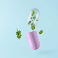 Pink pill with leafy green vegetable spinach floating above isolated pastel blue background. Minimal abstract agricultural concept. Natural food. Vitamins K, A, C, folate and antioxidants flavonoids.