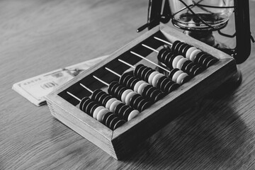 Old wooden abacus for counting money and dollars and an oil lamp nearby on a wooden table close-up black and white photo