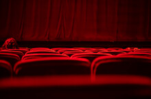 A Woman With Red Hair Sitting On A Velvet Red Seat At An Empty Theater