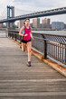 © Cavan Images - Female runner on waterfront in Brooklyn with Manhattan Bridge