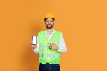 Wall Mural - Man in reflective uniform showing smartphone on orange background