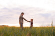 © Acronym - Farmer and his son in front of a sunset agricultural landscape. Man and a boy in a countryside field. Fatherhood, country life, farming and country lifestyle concept.