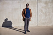 © baranq - Happy handsome man wearing coat and sunglasses standing against concrete wall during sunny afternoon looking at camera