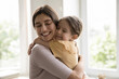 © fizkes - Cheerful happy young mother holding daughter kid in arms, tightening with cheek touches and closed eyes, hugging girl with love, tenderness, devotion, enjoying motherhood, closeness