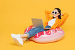 © ViDi Studio - Young woman wear summer clothes sit on rubber ring use laptop pc computer isolated on plain yellow background. Tourist travel abroad in free spare time rest getaway. Air flight trip journey concept.