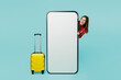 © ViDi Studio - Traveler happy woman wear casual clothes hold suitcase big huge blank screen mobile cell phone with area isolated on plain blue cyan background Tourist travel abroad in free spare time rest getaway..