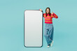 © ViDi Studio - Full body young woman wears bright casual clothes stand near big huge blank screen mobile cell phone smartphone with workspace mockup area show thumb up isolated on plain pastel blue cyan background