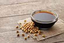 soy sauce in glass bowl with dry soybeans on wooden table