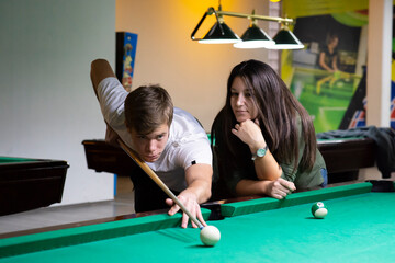 A guy and a young and beautiful woman are playing billiards in a club