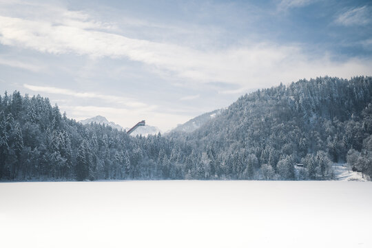 zugefrorener freibergsee in den alpen mit sicht auf die skiflugfschanze oberstdorf im allgäu