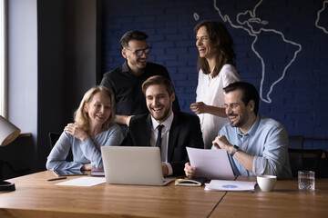 Wall Mural - Cheerful millennial business team working on project together, meeting at laptop, talking on video conference call, having fun, laughing, celebrating project success, enjoying teamwork, cooperation