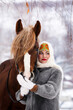 Portrait of a Russian beauty girl in traditional clothes with red big horse in forest winter